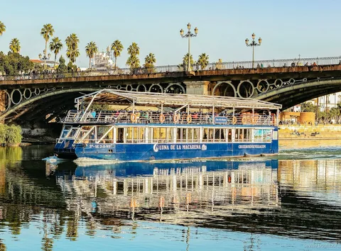 Blue cruise boat passing under the iron arches of Triana Bridge on a Seville boat tour on the Guadalquivir