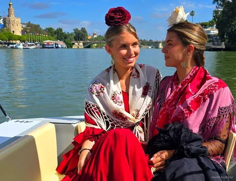 Two women in flamenco shawls and flower hairpieces on a private Seville boat tour with the Torre del Oro behind